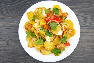 cooked fried potatoes with herbs and vegetables in a white plate on a wooden table