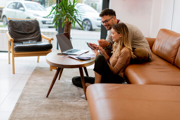 Young couple using laptop together while sitting on sofa at home
