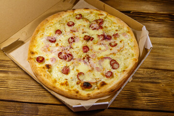 Delicious fresh pizza in cardboard box on a wooden table. Concept for home delivery of food, fast food, delivery of pizza