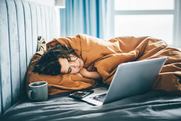 Tired woman with a laptop on a bed in the bedroom.