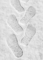 rhythmic boot prints on thin white snow in winter recede into the distance, vertical frame, ribbed...