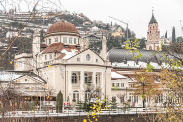 Kursaal oder Kurhaus on passeggiate (promenade) with duomo bell tower and Pulverturm (Torre Polveriera - Tower of powder) with snow in winter - Merano, South Tyrol, Italy - obrazy, fototapety, plakaty