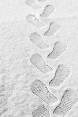 rhythmic boot prints on thin white snow in winter recede into the distance, vertical frame, ribbed protector, winter concept