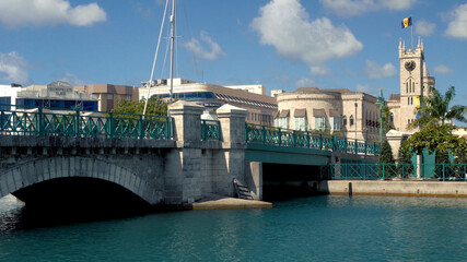 Bridgetown, Barbados: Chamberlain bridge with people passing and Parliament building with the flag on top of the tower in the background