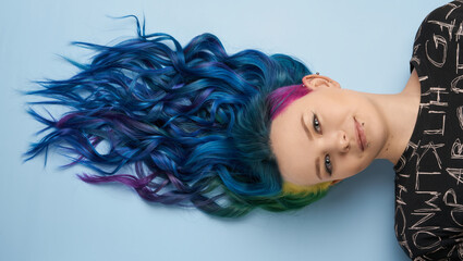Girl with creative blue coloring and a rainbow in her hair on a blue background. Modern minimalistic bright photography for advertising and social networks