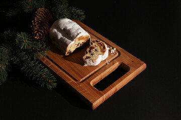 Beautiful Christmas cake decorated with fir branches and a pine cone on a wooden board. The background is black.