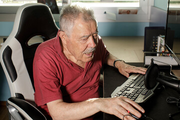 Anziano signore con un paolo è seduto di fronte al computer mentre di una camerata mentre utilizza...