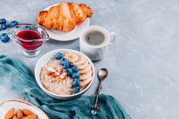 Healthy breakfast - oatmeal, croissant and coffee on a gray background, free space for text