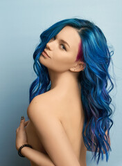 Naklejka premium Girl with creative blue coloring and a rainbow in her hair on a blue background. Modern minimalistic bright photography for advertising and social networks
