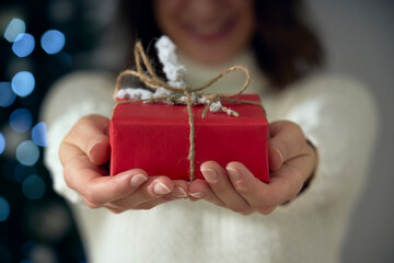 A woman holds in her hands a red and white gift to celebrate the holidays. A present for Christmas, birthday, thanksgiving, Valentine's Day and every anniversary. In the background a bokeh effect.