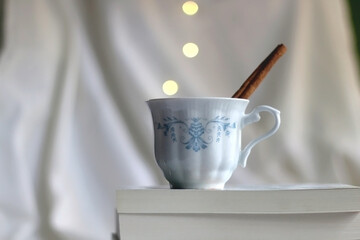 Stack of books and vintage cup with warm drink and cinnamon stick. Selective focus, bokeh lights.