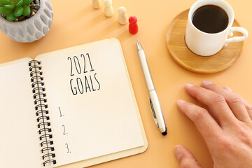 Business concept of top view 2021 goals list with notebook, cup of coffee over pastel yellow...
