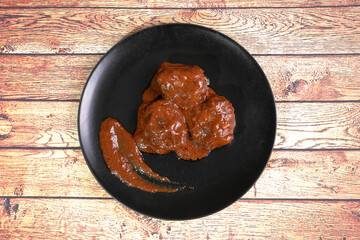 Braised pork cheeks in red wine sauce on black plate on wooden table