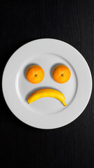In the form of a disgruntled face, tangerines and a banana on a plate. Fruit imitating a sad smiley.