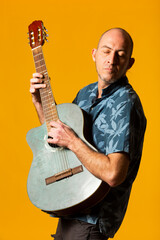 Portrait of a Musician while plying his blue acoustic guitar against a yellow background