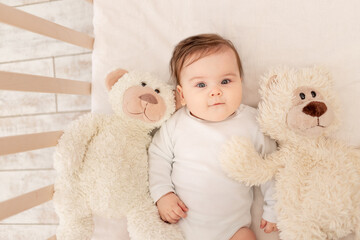 the baby is six months old in a crib in a white bodysuit with a Teddy bear