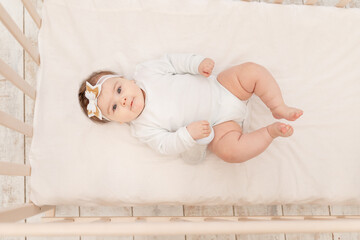 baby six months in bed with a bottle of water in a white bodysuit