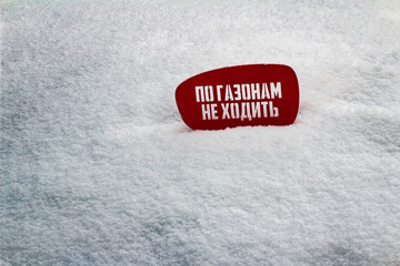 Red notice board on white snow with text in Russian do not walk on the lawns