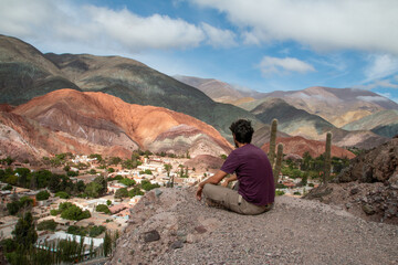 Man sitting in the mountains, looking at the town of Purmamarca.
