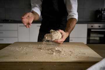 The hands of the strong man knead the dough from which they will make bread, pasta, cake or pizza. In his kitchen he carries on the tradition of homemade pasta. A cloud of white flour flies like dust.