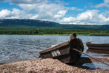 wooden boat on the shore of the lake in cloudy summer day with mountain on the background