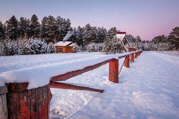 house on the edge of the winter forest with wooden fence