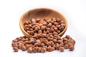 Hazelnuts spilled from wooden bowl on white background. Solid ripe Hazelnuts