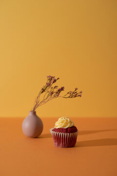 A single tiny velvet cupcake and vase with little pretty sprigs of flowers on yellow minimalistic background
