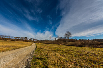 dirt road and a hill with forest and fine clouds at the sky