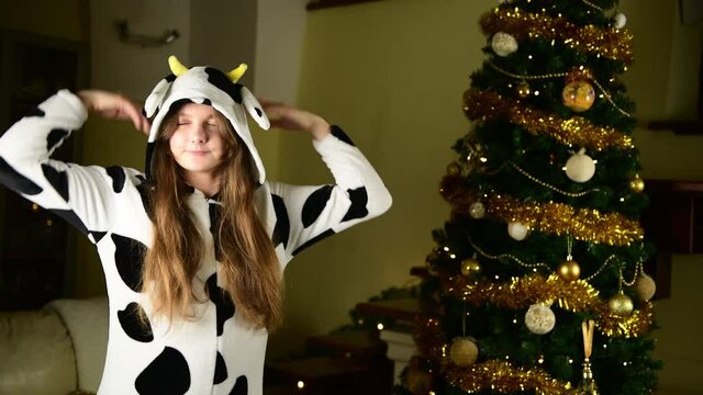 Funny girl in bull cow pajamas dancing near Christmas tree with positive surprised face expression. Young woman celebrating Happy New Year, Happy Dancing Cow. Crazy Year, Year of the bull 2021