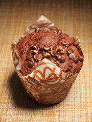A cupcake, sprinkled with pieces of chocolate, is on the table.
