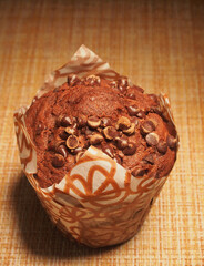 A cupcake, sprinkled with pieces of chocolate, is on the table.