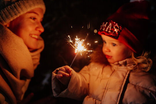 Daughter and mother kindling sparkler at night