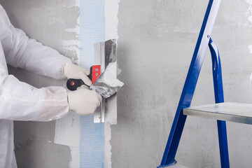 repairman seals a crack in the wall with mortar and mesh, close-up