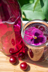 Summer lemonade with cherry berries and violet flower in a glass in the garden. The concept of healthy fruit drinks