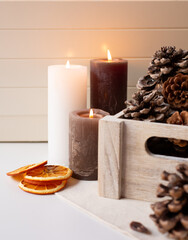 Three lighted candles and cedar cones in a wooden box and dry orange slices are on a light background.