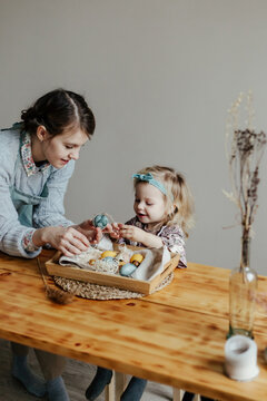 Funny little girl with mother decorating egg with sticker on Easter