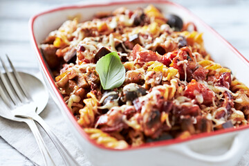 Baked fusilli pasta with cherry tomatoes, olives and mozzarella cheese. Bright wooden background. Close up. 