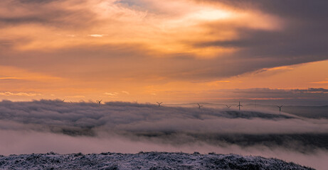 Electric generating windmills appearing through a cloud inversion at sunset, Slieveanorra Mountain,...