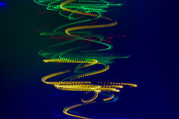 on a dark blue background there is a spiral of yellow and green lights removed at a long shutter speed. Horizontal photo, abstract background.