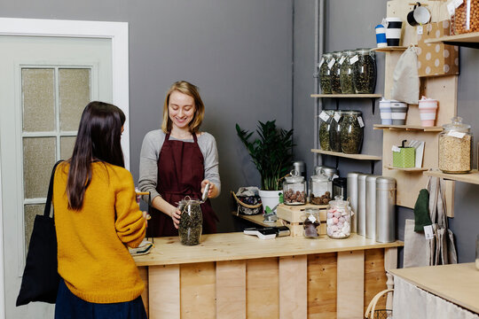Seller offering buyer tea to choose standing behind counter in organic shop