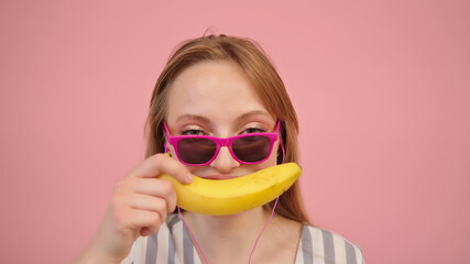 Portrait of funny caucasian blond woman holding banana over her lips. Isolated on pink background. High quality photo