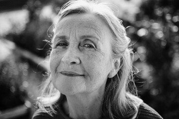Black and white portrait of senior woman with grey hair and face with wrinkles outdoors relaxing at the park