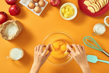 Woman hands breaking an egg to separate egg white and yolks and egg shells at the background