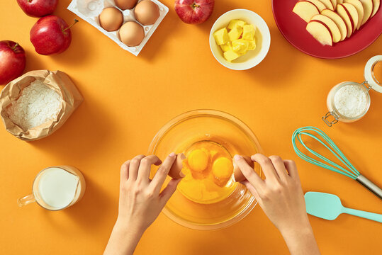 Woman hands breaking an egg to separate egg white and yolks and egg shells at the background