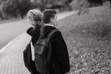 Schoolchildren, a boy and girl in medical masks walk in the city park.
