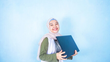 Portrait of an happy hijab girl holding laptop computer and celebrating success isolated over blue background
