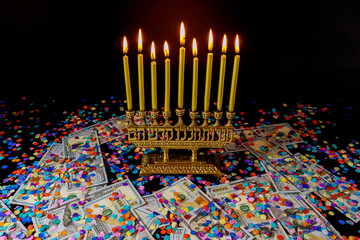 Golden candles on menorah and confetti with money on black background. Jewish holiday Hanukkah.