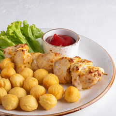 Chicken pieces on a wooden skewer with potato balls and ketchup