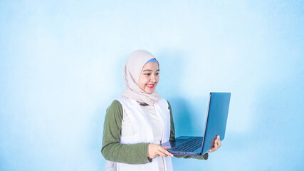 Cheerful asian hijab woman having a videocall while standing on a floor with laptop computer